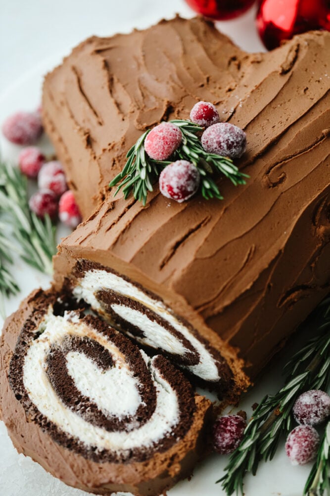 Show off your holiday spirit by baking this amazing yule log cake! A chocolate cake rolled with a cream cheese filling and topped with a chocolate ganache... It doesn't get much better than this! A yule log cake with a slice showing the inside swirl.