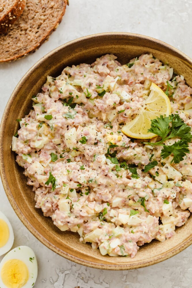 This amazing ham salad is filled with so much flavor! Super simple and easy to make, use some leftover ham and you can whip this up for lunch in under 10 minutes!ย A bowl of ham salad garnished with a lemon.