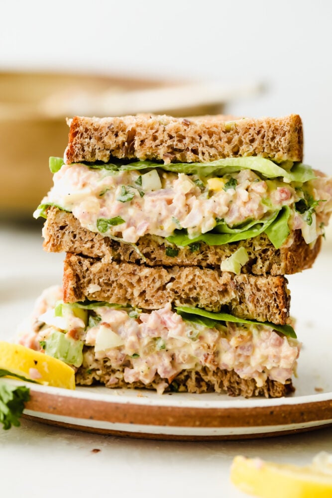 This amazing ham salad is filled with so much flavor! Super simple and easy to make, use some leftover ham and you can whip this up for lunch in under 10 minutes!ย A ham salad sandwich on a plate stacked 2 high.