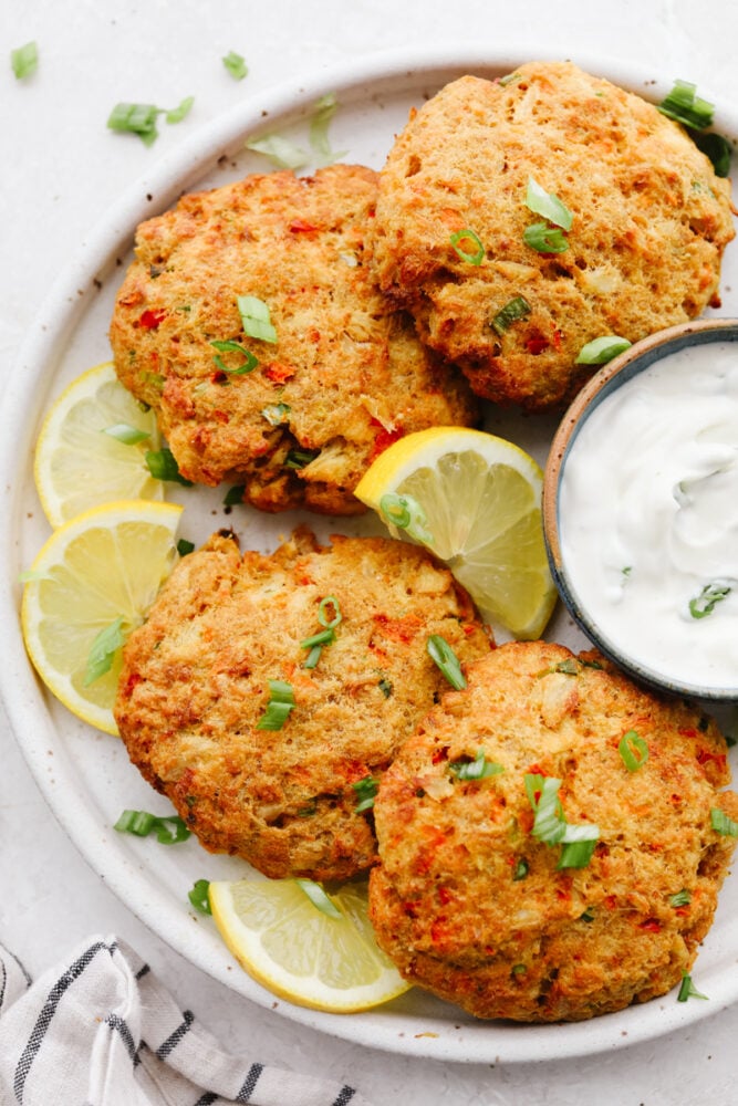Air fryer crab cakes are an amazing appetizer that comes together in a snap! Each bite is tender, savory, and packed with all the crab flavor you crave! 4 air fryer crab cakes on a white plate with lemon and green onion garnish.