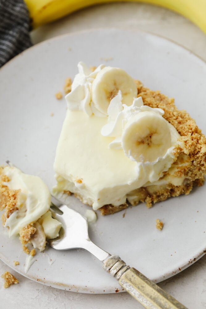 You don't even need an oven to make this banana cream cheesecake! This has a crust and a perfectly creamy filling. Top it with some whipped cream and fresh bananas and you won't be able to stop at one slice! A slice of banana cream cheesecake with a fork cutting a bite.