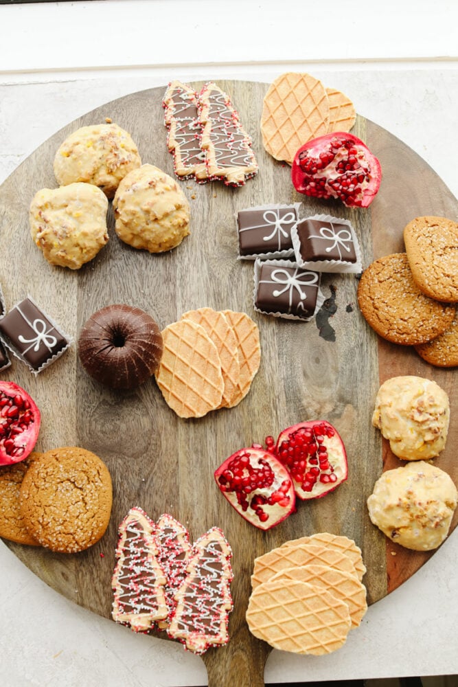 If you are looking for a Christmas dessert to impress your guests then this charcuterie board is it! Stunning and delicious, this board is full of candy, chocolate, cookies, and fruit for the holiday season!ย A wooden board with pasties being added to it.
