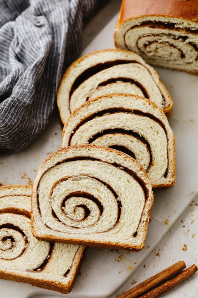 This bread not only tastes amazing but those thick cinnamon swirls make it gorgeous enough to impress any guest! WIth the perfectly golden outside and delicious cinnamon flavor on the inside, you will come back to this again and again! Slices of cinnamon swirl bread on a cutting board.