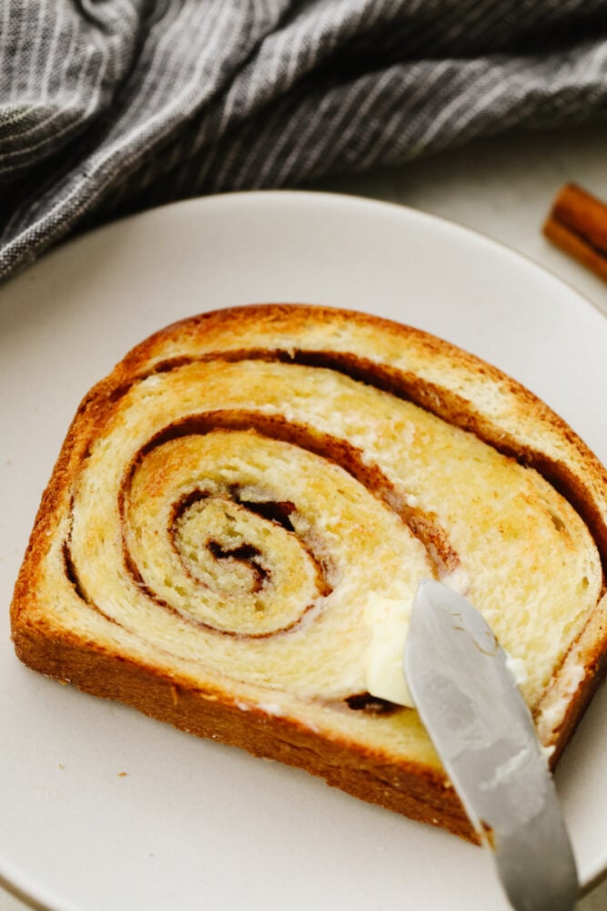 This bread not only tastes amazing but those thick cinnamon swirls make it gorgeous enough to impress any guest! WIth the perfectly golden outside and delicious cinnamon flavor on the inside, you will come back to this again and again! Butter being spread on a slice of the bread.