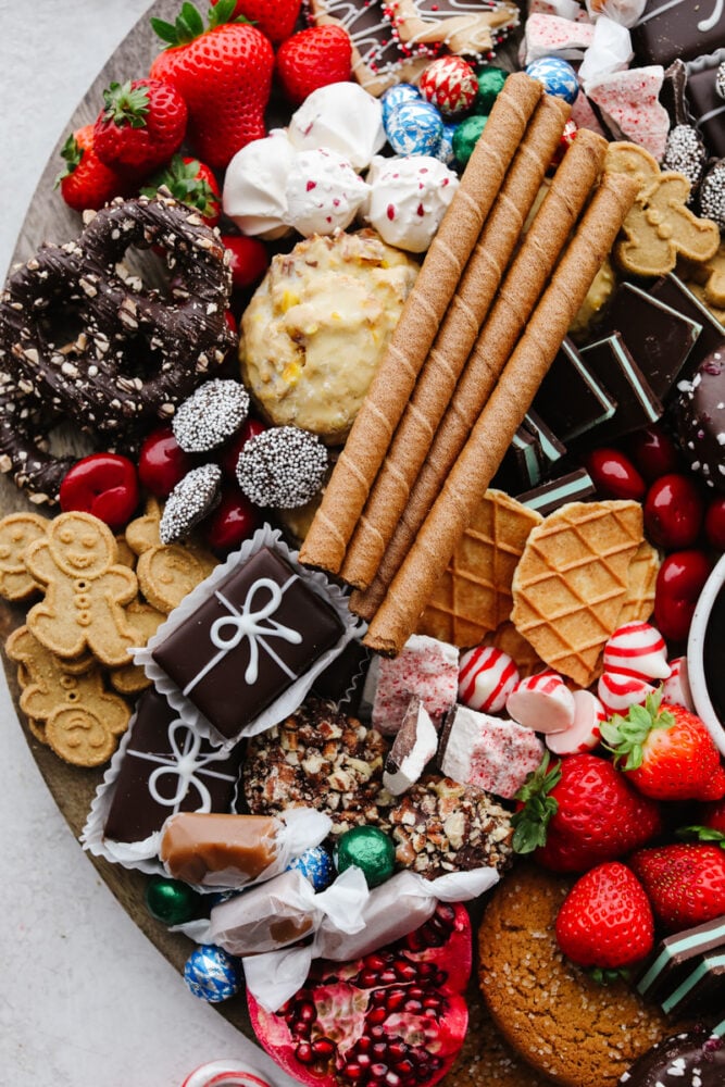 If you are looking for a Christmas dessert to impress your guests then this charcuterie board is it! Stunning and delicious, this board is full of candy, chocolate, cookies, and fruit for the holiday season!ย A zoomed in shot of some chocolates, cookies, fruit and candy on a wooden board.