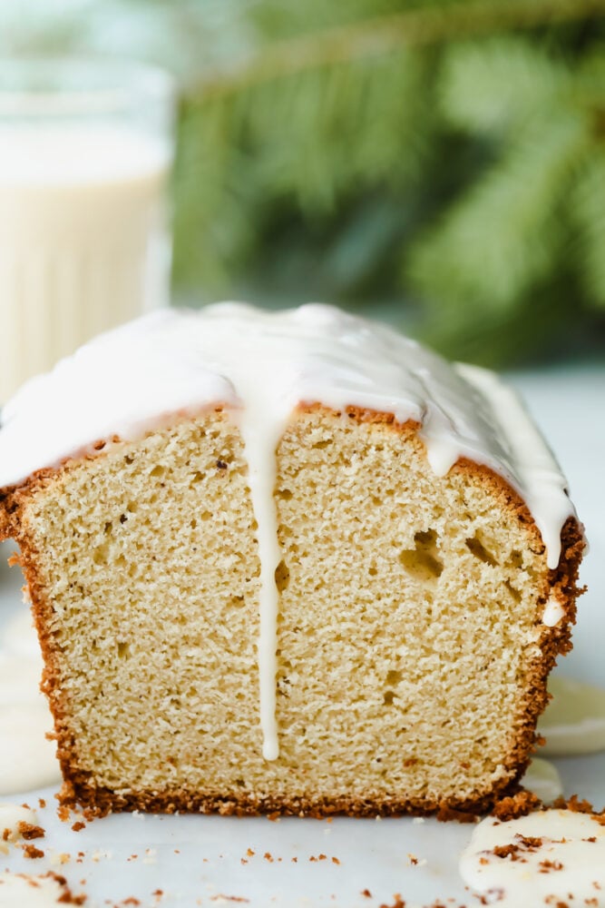The subtle taste of eggnog in this quick bread is amplified with the ooey-gooey eggnog glaze that is drizzled on top. It's the perfect simple and easy holiday treat! A side view of a loaf of eggnog quick bread with an eggnog glaze dripping down.