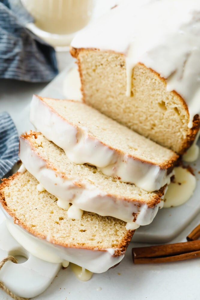 The subtle taste of eggnog in this quick bread is amplified with the ooey-gooey eggnog glaze that is drizzled on top. It's the perfect simple and easy holiday treat! A loaf of eggnog quick bread sliced with an eggnog glaze on top.