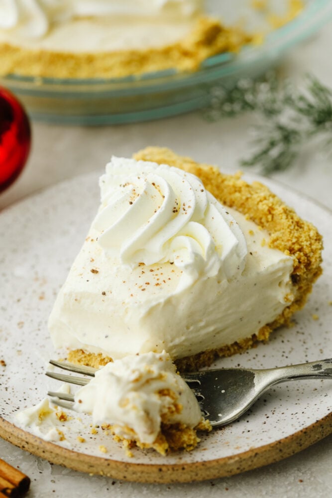 No-bake eggnog pie really takes the festivities of the season up a notch! Creamy, delicious, and made with the perfect eggnog flavor, this pie will be a hit at all of your parties! A slice of eggnog pie on a plate with a fork cutting into it.