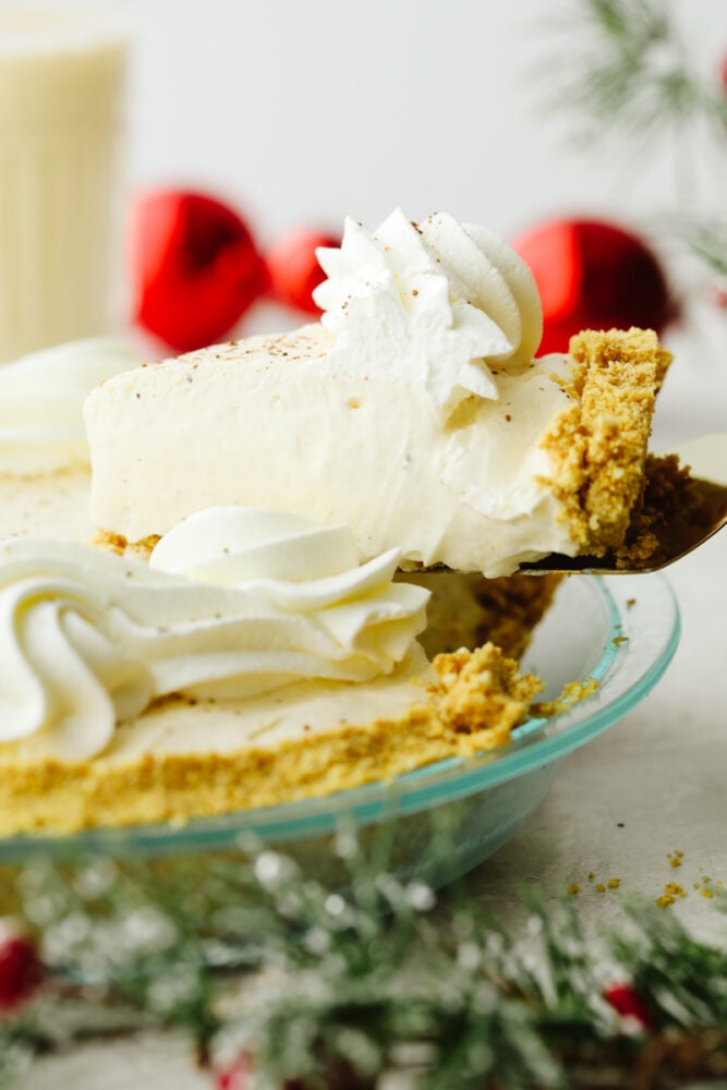 No-bake eggnog pie really takes the festivities of the season up a notch! Creamy, delicious, and made with the perfect eggnog flavor, this pie will be a hit at all of your parties! A slice of pie being taken out of the pie pan.