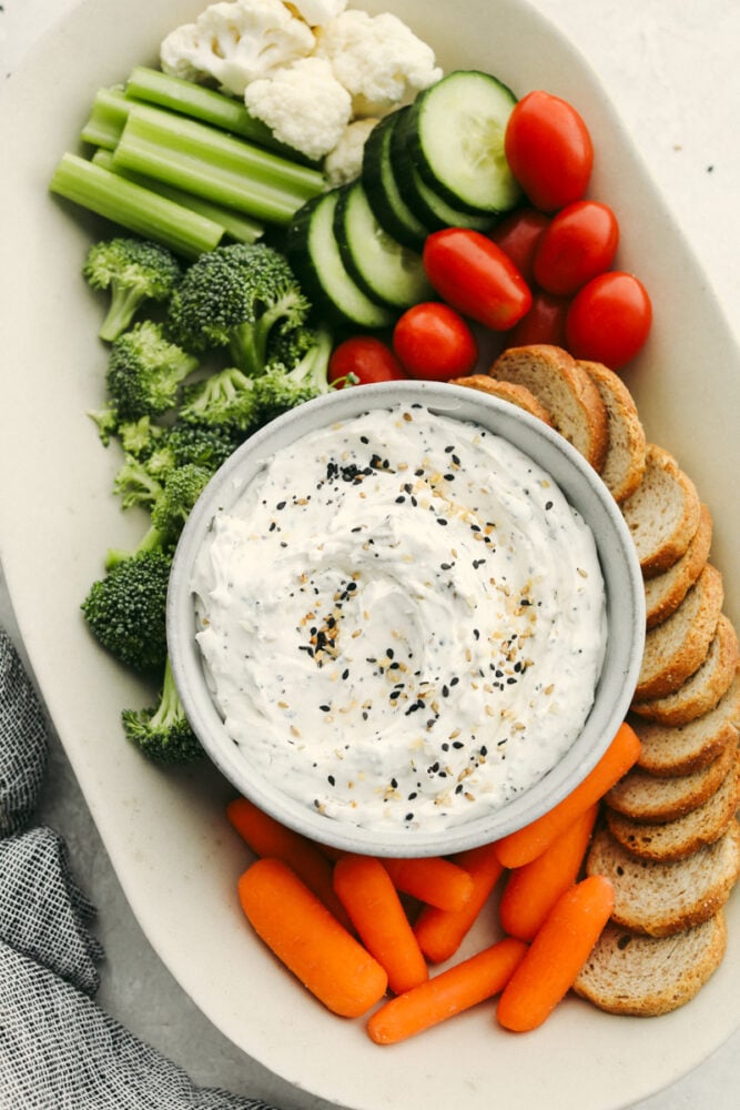 This creamy everything bagel dip is THE BEST dip out there! Bring it as an appetizer that everyone will enjoy and it will fly off of the table! A platter with veggies and bread and a bowl of everything bagel dip.