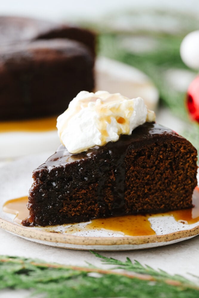 This warm gingerbread cake is made of up delicious and classic holiday flavors. Topped with a homemade caramel sauce, it melts in your mouth and flies off of the table. Your guests will love it! A slice of gingerbread cake with a dollop of whipped cream.