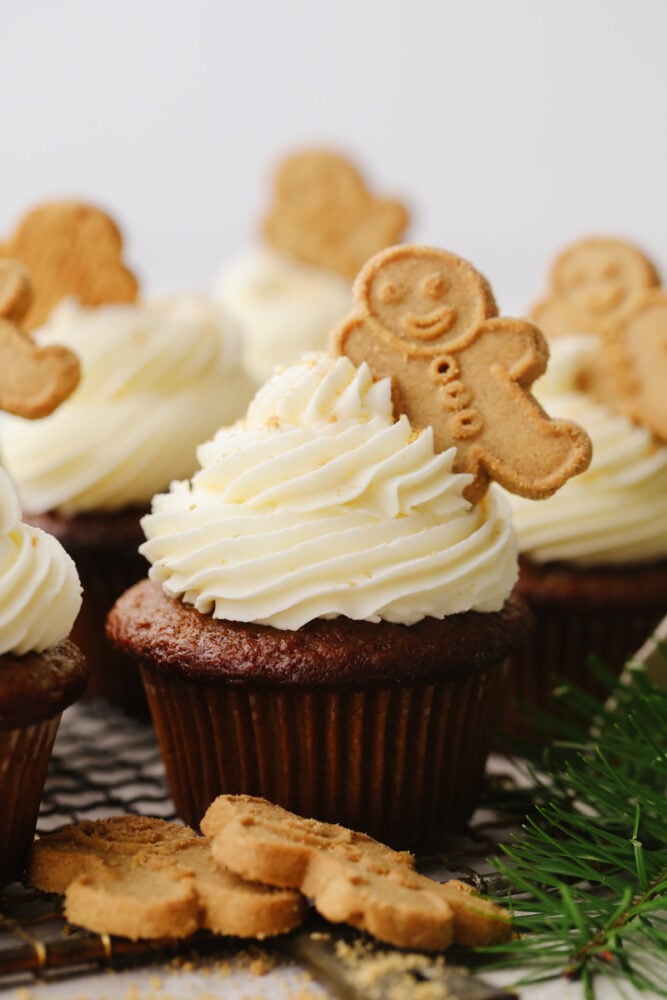 These gingerbread cupcakes are fun, festive, and perfect for the holiday season! It's a moist and tender gingerbread flavored cupcake that is topped with a delicious white chocolate buttercream that everyone will go crazy over. A gingerbread cupcake with frosting and a gingerbread cookie on top.