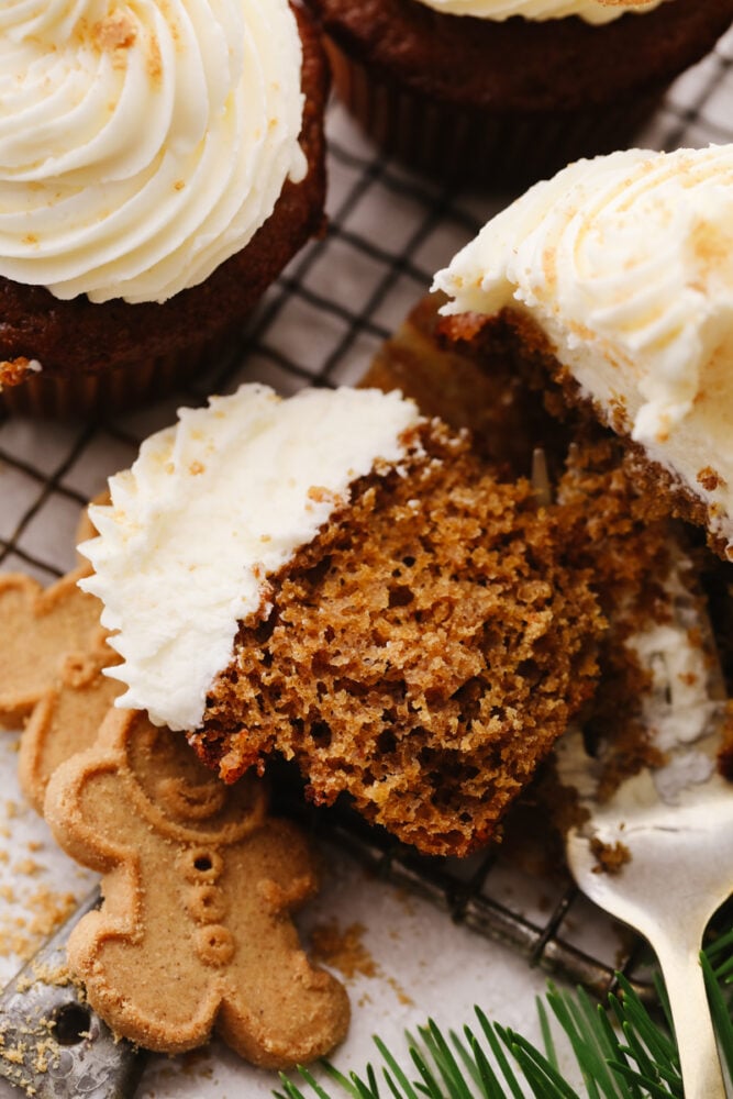 These gingerbread cupcakes are fun, festive, and perfect for the holiday season! It's a moist and tender gingerbread flavored cupcake that is topped with a delicious white chocolate buttercream that everyone will go crazy over. A gingerbread cupcake on a cooling rack being cut open with a fork.