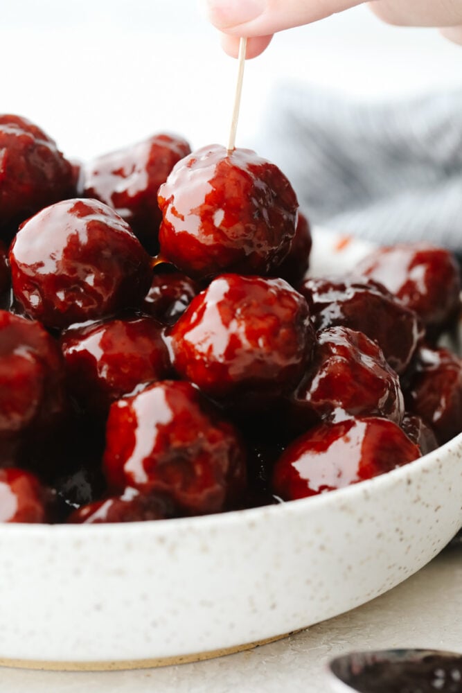 These grape jelly meatballs are so simple and easy and my whole family loves them! They pack so much flavor and are the perfect meal or appetizer for any occasion! A bowl of grape jelly meatballs with a toothpick sticking in one of them.