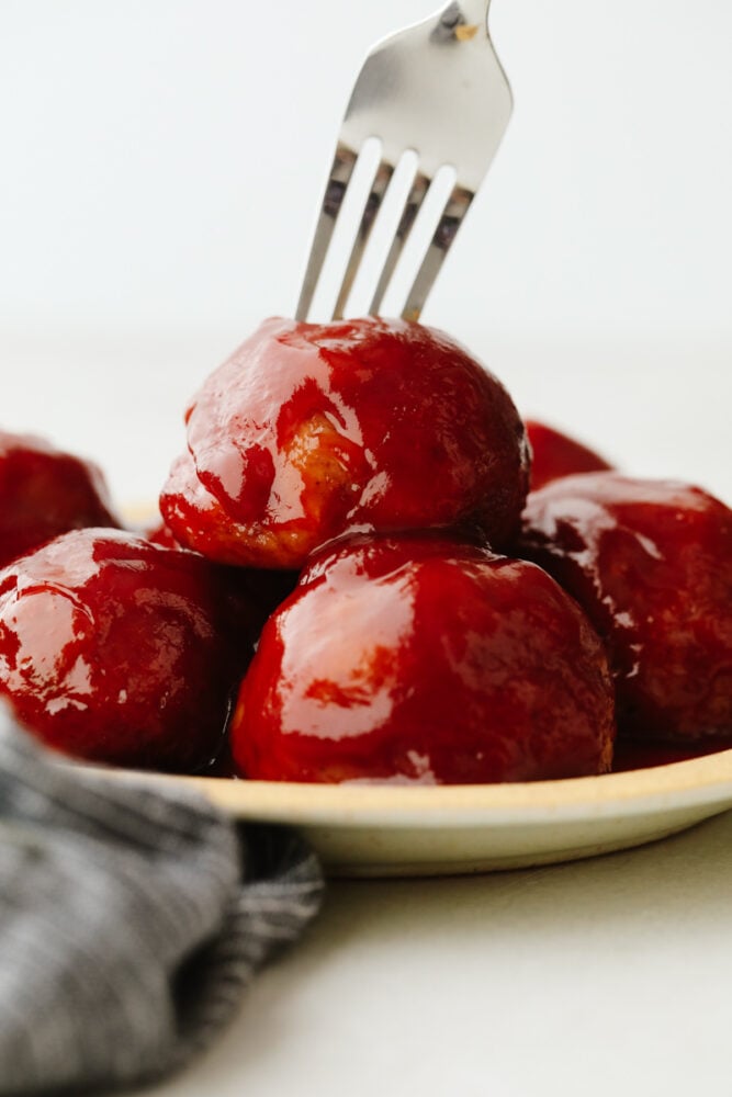 This tasty midwestern dish is ready to win the hearts of your family! With a thick, zesty brown sugar glaze, these delicious ham balls are the best addition to your dinner rotation! Closeup of ham balls, one being stuck with a fork.