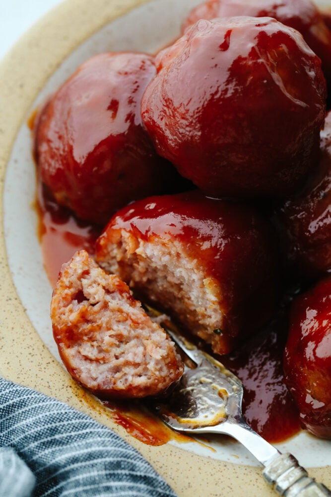 This tasty midwestern dish is ready to win the hearts of your family! With a thick, zesty brown sugar glaze, these delicious ham balls are the best addition to your dinner rotation! Closeup of a ham ball being cut in half.