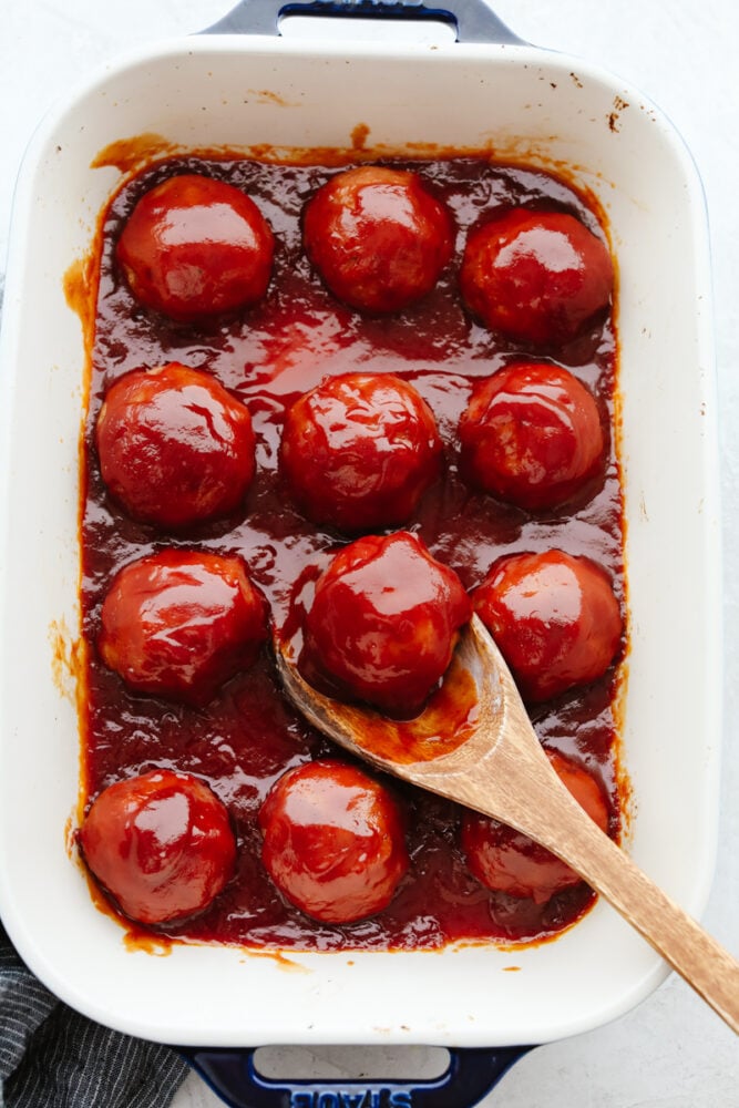 This tasty midwestern dish is ready to win the hearts of your family! With a thick, zesty brown sugar glaze, these delicious ham balls are the best addition to your dinner rotation! 12 meatballs in a white casserole dish.