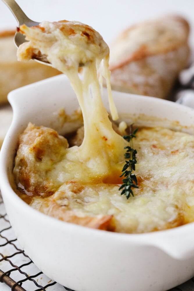 French onion soup is a classic that you can now easily cook in your instant pot! Flavored to perfection and topped with delicious cheese this soup will warm you up on any cold winter day. French Onion soup in a bowl topped with cheese and being scooped out with a spoon.
