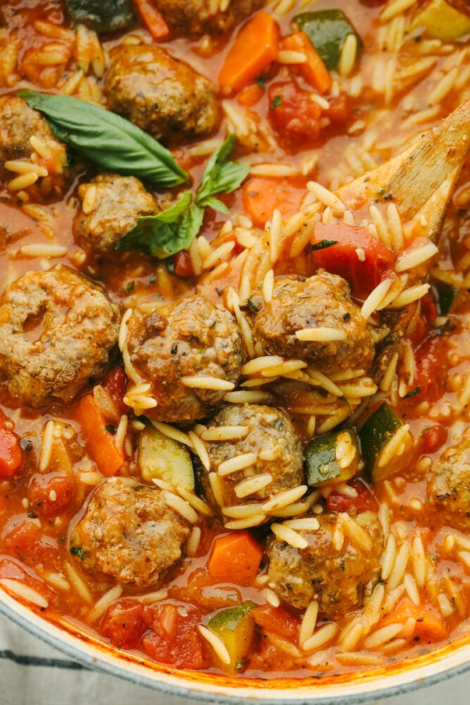 This meatball soup is hearty and full of amazing flavor. This only takes about 30 minutes to cook up and can be made with homemade or frozen meatballs! It's a MUST TRY recipe for sure! Meatball soup being dished out with a wooden spoon.