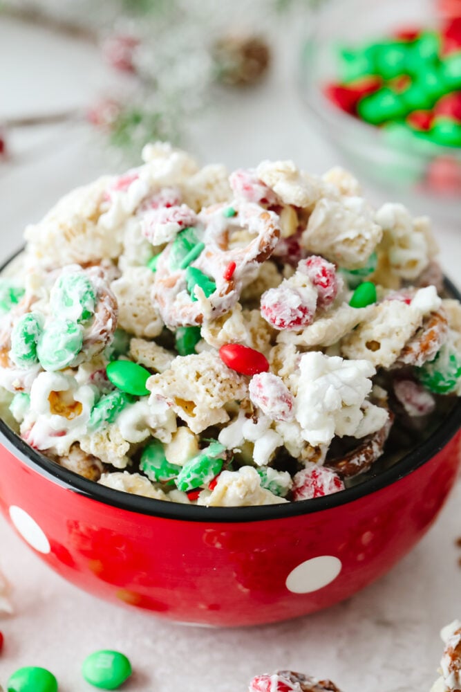 This reindeer food is the most addicting mixture of treats! It's the perfect combo of sweet and salty and ideal for any holiday gathering! Chex, pretzels, m&m's, peanuts, and popcorn covered with white chocolate and sprinkles in a red, polka dot bowl.