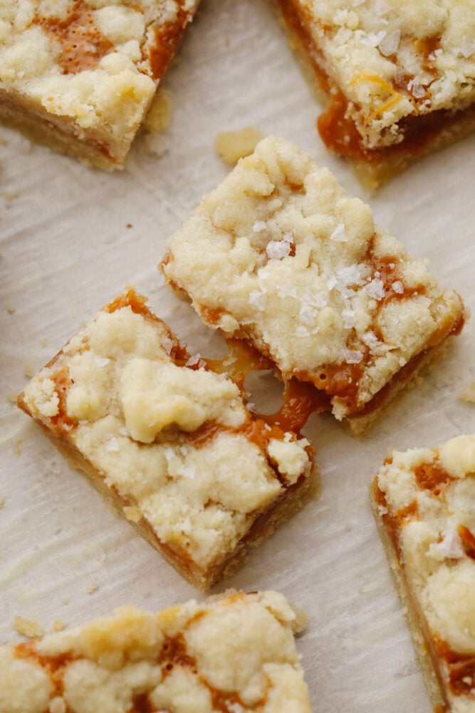 Salted caramel butter bars are the perfect easy-to-make dessert. With a buttery and crumbly shortbread crust that is topped with a smooth layer of caramel, there will be a little bit of sweet and savory in each bite! A broken salted caramel bar with caramel dripping.