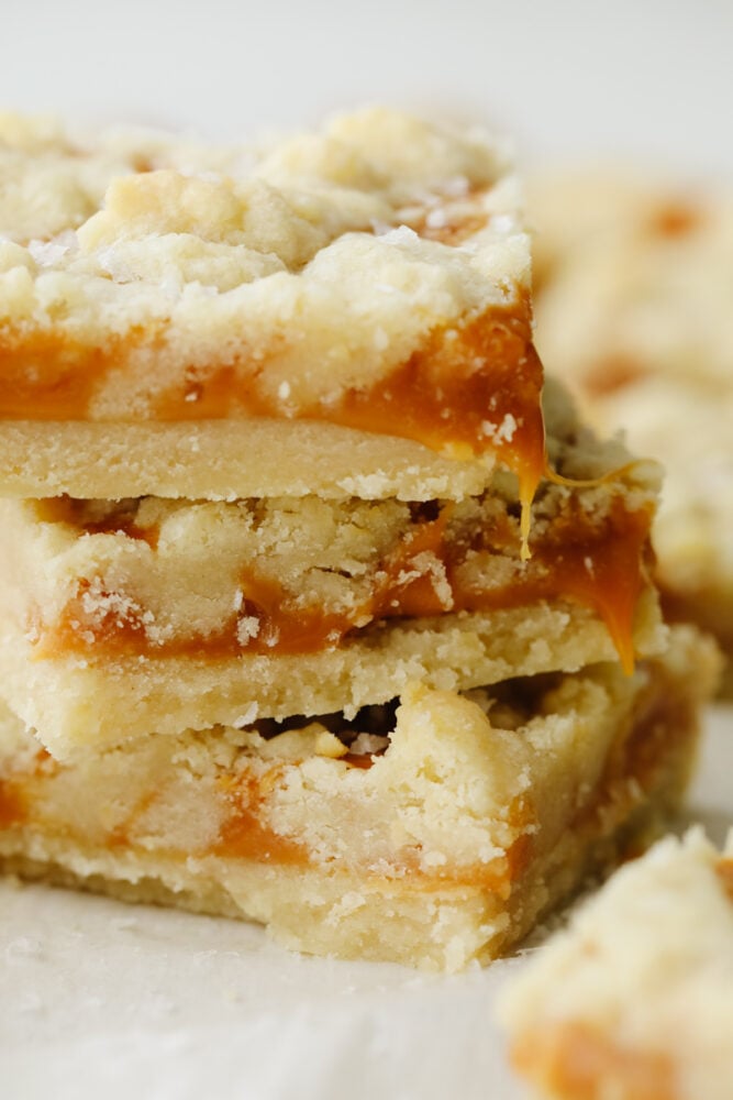 Salted caramel butter bars are the perfect easy-to-make dessert. With a buttery and crumbly shortbread crust that is topped with a smooth layer of caramel, there will be a little bit of sweet and savory in each bite! A zoomed in stack of salted butter caramel bars.