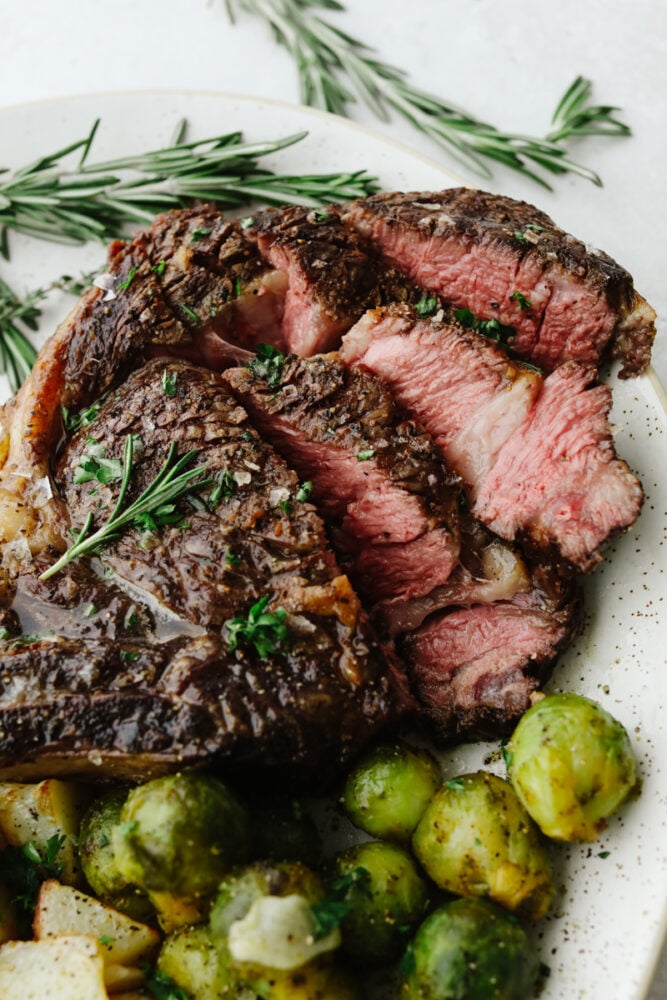 This tomahawk steak is juicy, tender, and filled with insanely delicious flavor! Make it your main dish for any occasion and your guests will keep coming back for more! A sliced tomahawk steak on a plate with some brussel sprouts.