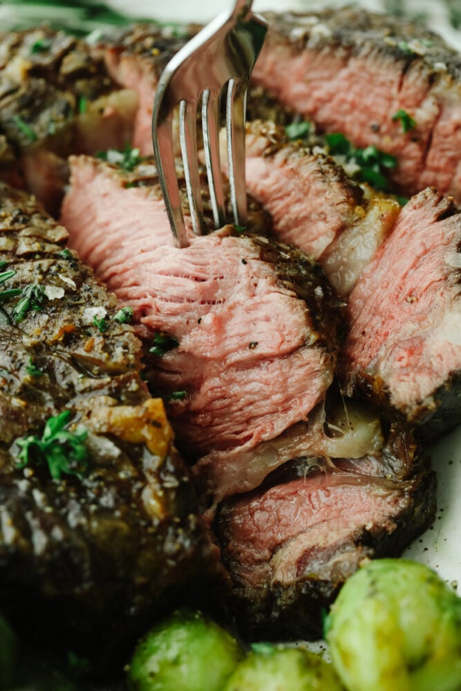 This tomahawk steak is juicy, tender, and filled with insanely delicious flavor! Make it your main dish for any occasion and your guests will keep coming back for more! A sliced steak with a fork in it.
