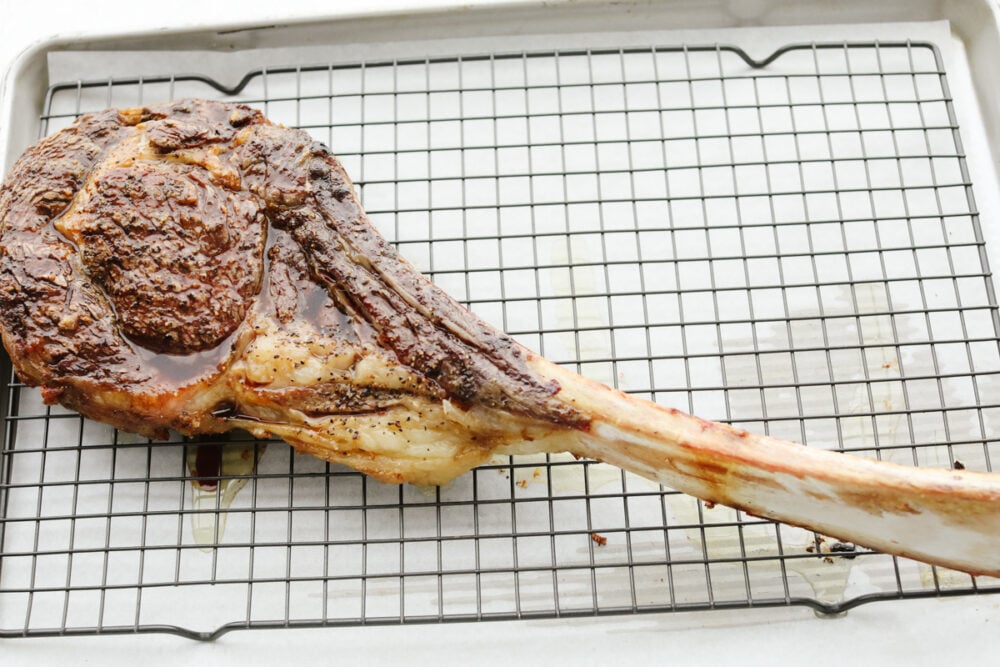This tomahawk steak is juicy, tender, and filled with insanely delicious flavor! Make it your main dish for any occasion and your guests will keep coming back for more! A tomahawk steak on a cooling rack, resting.