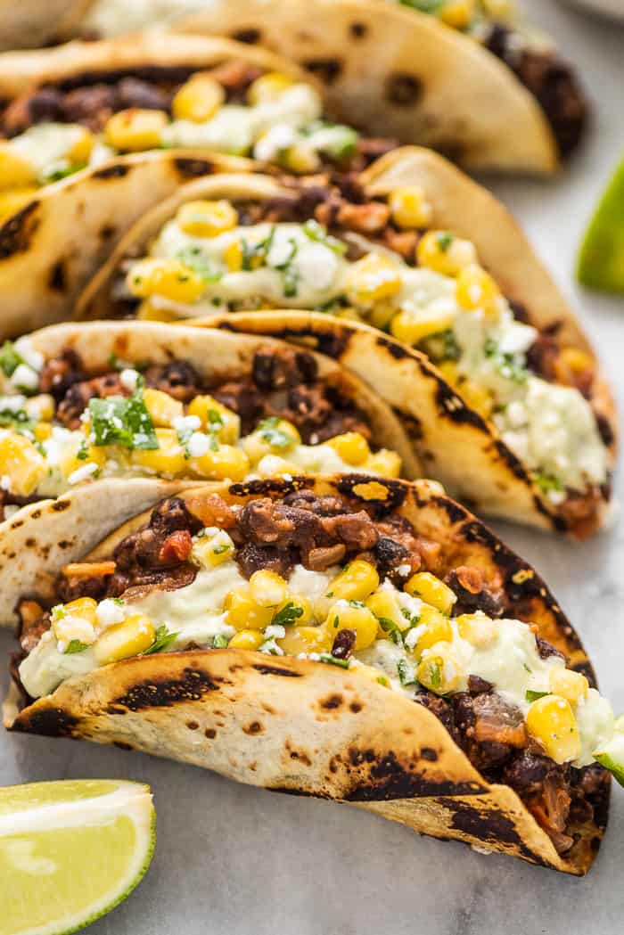 Black bean tacos are an easy-to-make and healthy vegetarian dinner that the whole family will love. Flavorful black beans are spooned inside soft tortillas and topped with simple corn salsa and some avocado crema. a close up of black bean tacos