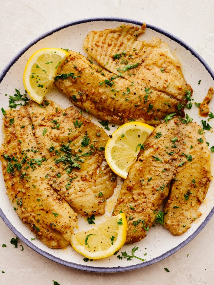 Using an air fryer and Cajun spices is the best way to cook up this tender fish! This air fryer cajun garlic butter tilapia is so easy and delicious, it's sure to become a new favorite lunch! Cooked air fryer tilapia with lemon garnish on a white plate.