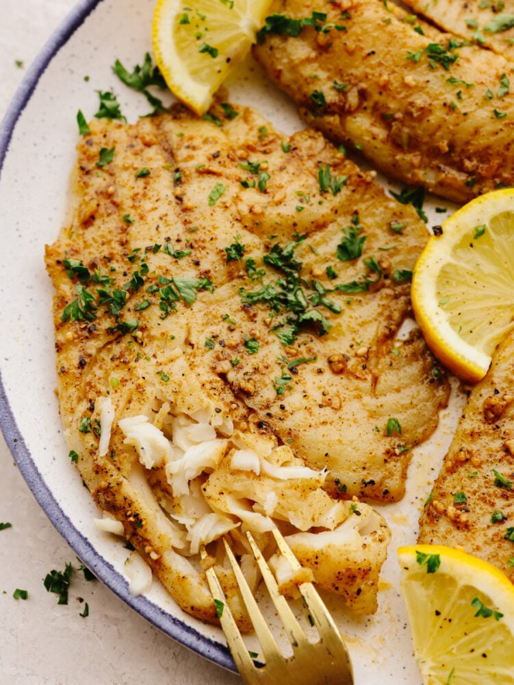 Using an air fryer and Cajun spices is the best way to cook up this tender fish! This air fryer cajun garlic butter tilapia is so easy and delicious, it's sure to become a new favorite lunch! Breaking off a piece of a tilapia fillet with a fork.