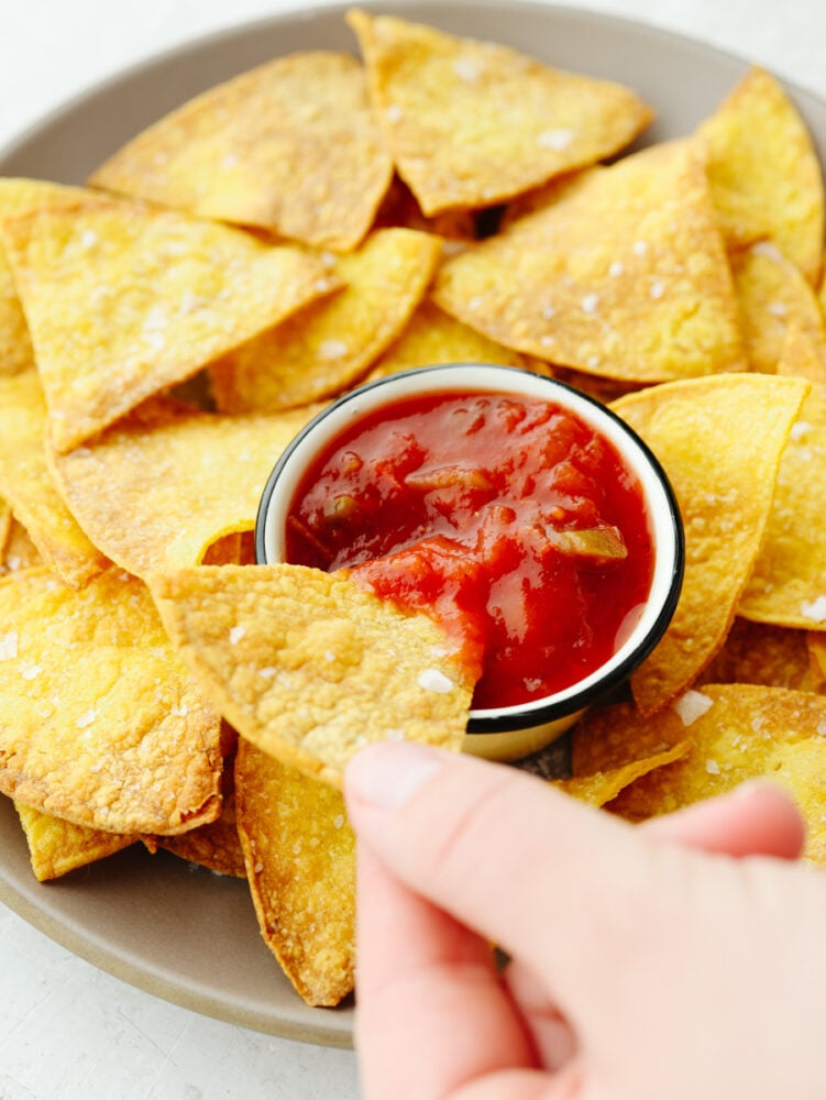 Air fryer tortilla chips are the perfect addition to all of your favorite salsas and dips! Once you try homemade chips, you won't want them any other way! Air fryer tortilla chips on a light brown plate served with salsa.