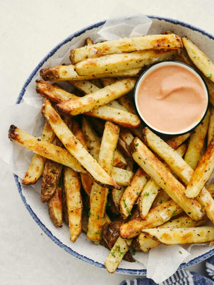 These golden, baked fries are perfectly crispy without the mess of deep-frying! Tossed with oil and tasty Italian herbs, these are sure to become a new family favorite! Fries on a white plate served with fry sauce.