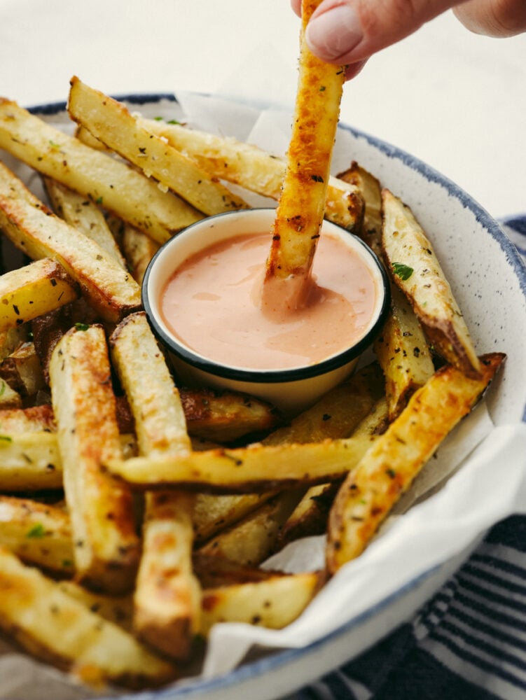These golden, baked fries are perfectly crispy without the mess of deep-frying! Tossed with oil and tasty Italian herbs, these are sure to become a new family favorite! Dipping a fry into fry sauce.
