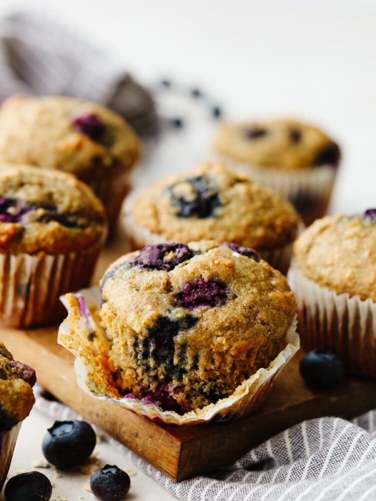 These blueberry oatmeal muffins are a healthy, hearty snack or breakfast loaded with whole grains and bursting berries! They're a delicious way to give you energy throughout your busy days! Blueberry muffins on a cutting board, one partially unwrapped.