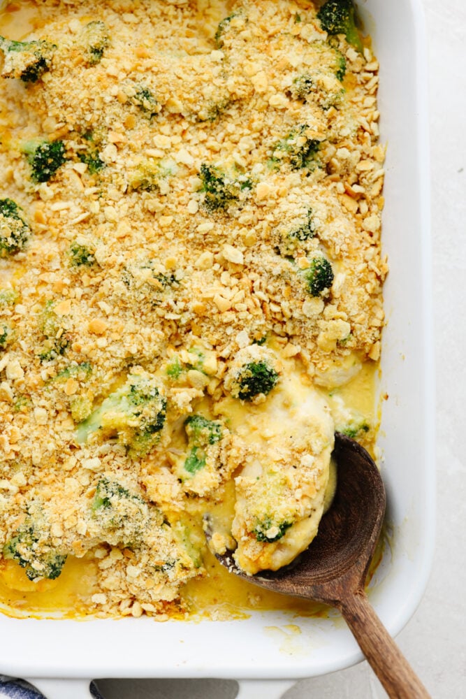 Comfort food at its finest, this broccoli cheddar chicken will fill you right up! Insanely delicious and straightforward to make, this is a dinner your entire family will go crazy over! A casserole dish with a wooden spoon serving some broccoli cheddar chicken.