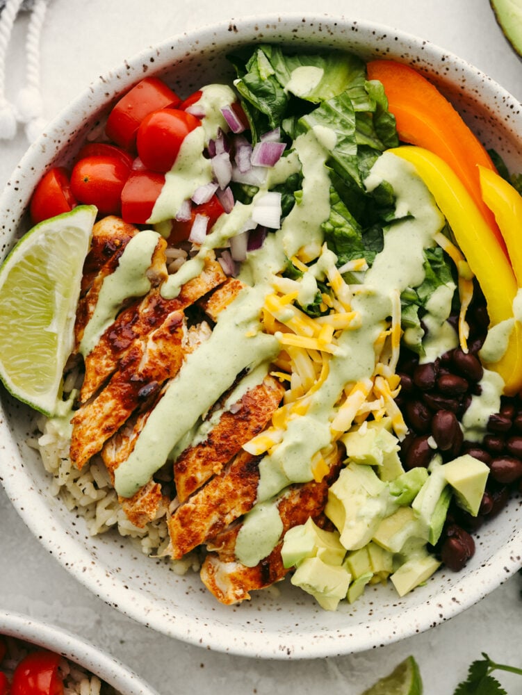 Packed with fresh veggies, rice, and juicy seared chicken, burrito bowls are the most delicious way to fuel your body! Topped off with creamy cilantro ranch, this is the perfect lunch filled with amazing flavor and texture. Closeup of a burrito bowl topped with cilantro ranch dressing.