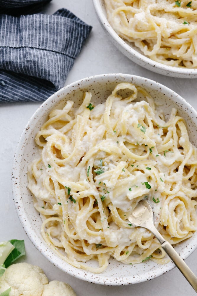 This cauliflower alfredo sauce is rich, creamy, and healthy! With this sauce, you get all of that insanely delicious flavor without the heavy cream. It's so good that you will want to put it on everything! Bowls of cauliflower sauce on fettuccine.