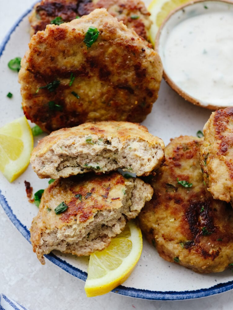 These chicken patties are crispy and perfectly browned on the outside and juicy and tender on the inside. They are a delicious addition to any meal for any occasion! Chicken patties on a platter with tartar sauce. One of the patties is broken open.