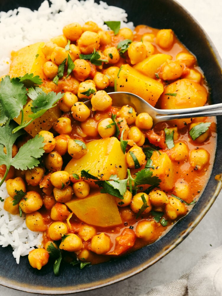 Chickpea curry is easy, healthy, and bursting with flavor! You'll be hooked after one bite of this hearty curry loaded with garlic, spices, and tender pieces of potato. Closeup of curry served over rice in a stoneware dish with cilantro garnish on top.