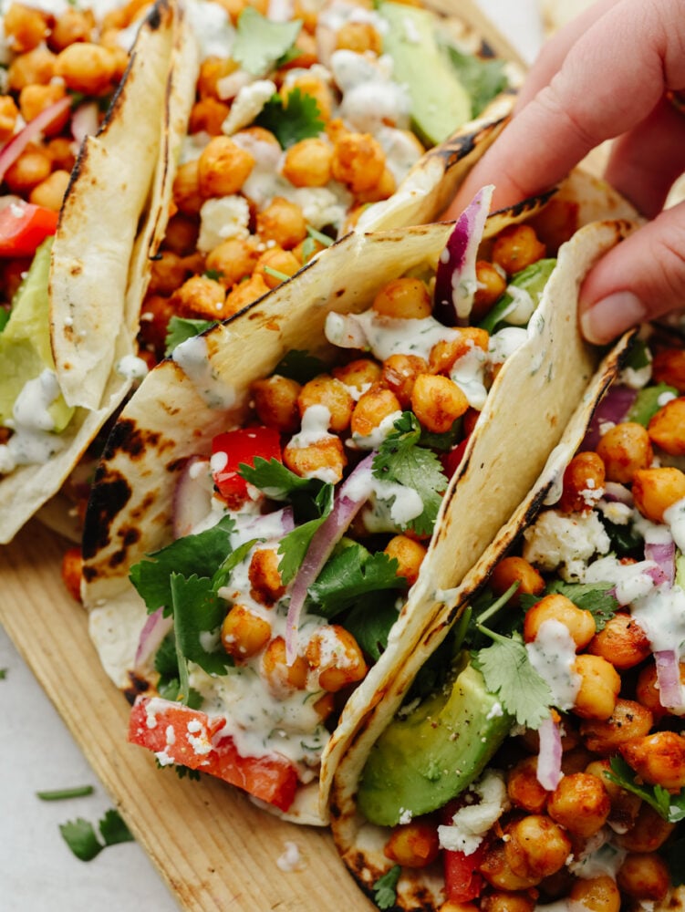 Chickpea tacos are a great way to get your daily protein and all the Tex-Mex flavors that you crave! These flavorful tacos are loaded with fresh veggies and topped off with a creamy cilantro drizzle!ntro drizzle! Closeup of a chickpea taco topped with cilantro being held.