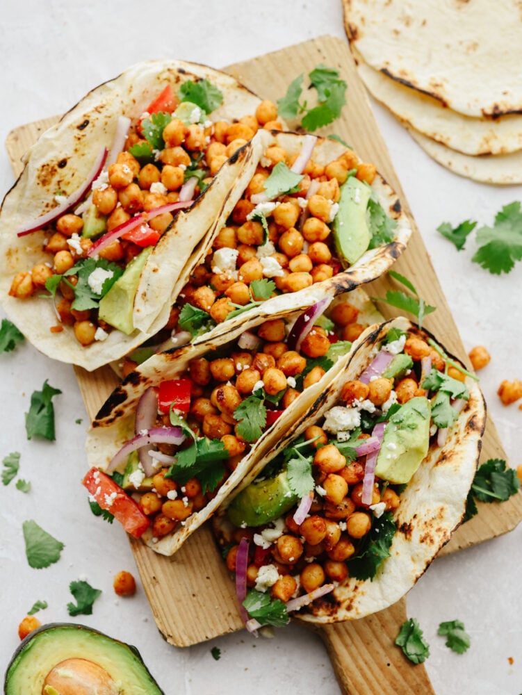 Chickpea tacos are a great way to get your daily protein and all the Tex-Mex flavors that you crave! These flavorful tacos are loaded with fresh veggies and topped off with a creamy cilantro drizzle! Chickpea tacos on a wooden serving board.