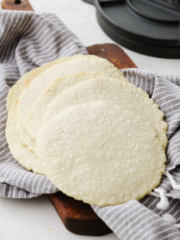 Homemade corn tortillas only have three ingredients and are a cinch to make! These guys are crispy on the edges, soft on the inside, and full of corn flavor. A stack of corn tortillas on a dish towel.