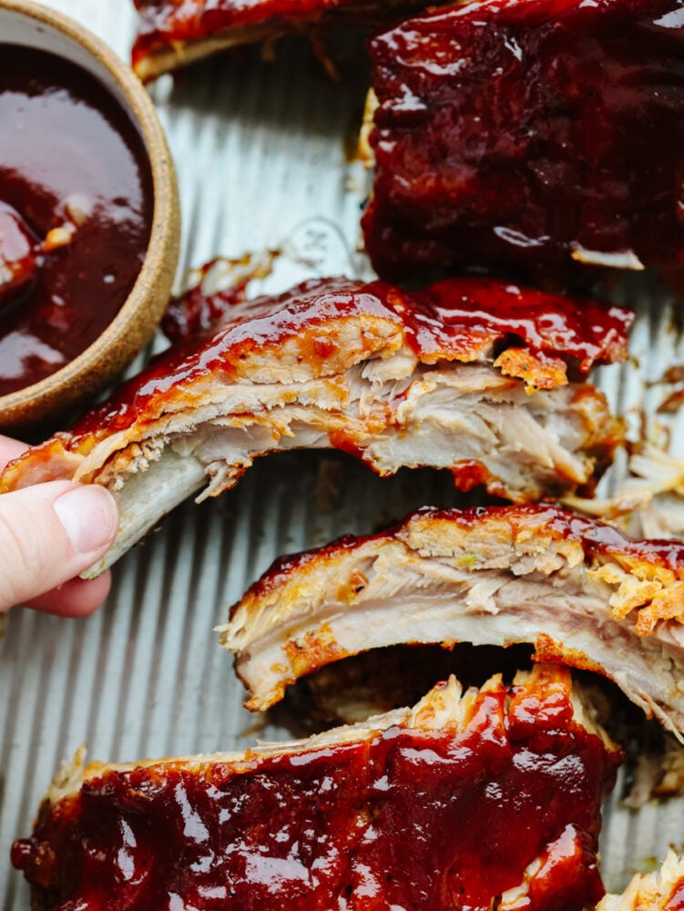 These Instant Pot ribs are fall off the bone tender, easy to make, and loaded with flavor! Enjoy straight them out of the pressure cooker slathered with your favorite bbq sauce! A hand picking up an instant pot rib to eat.