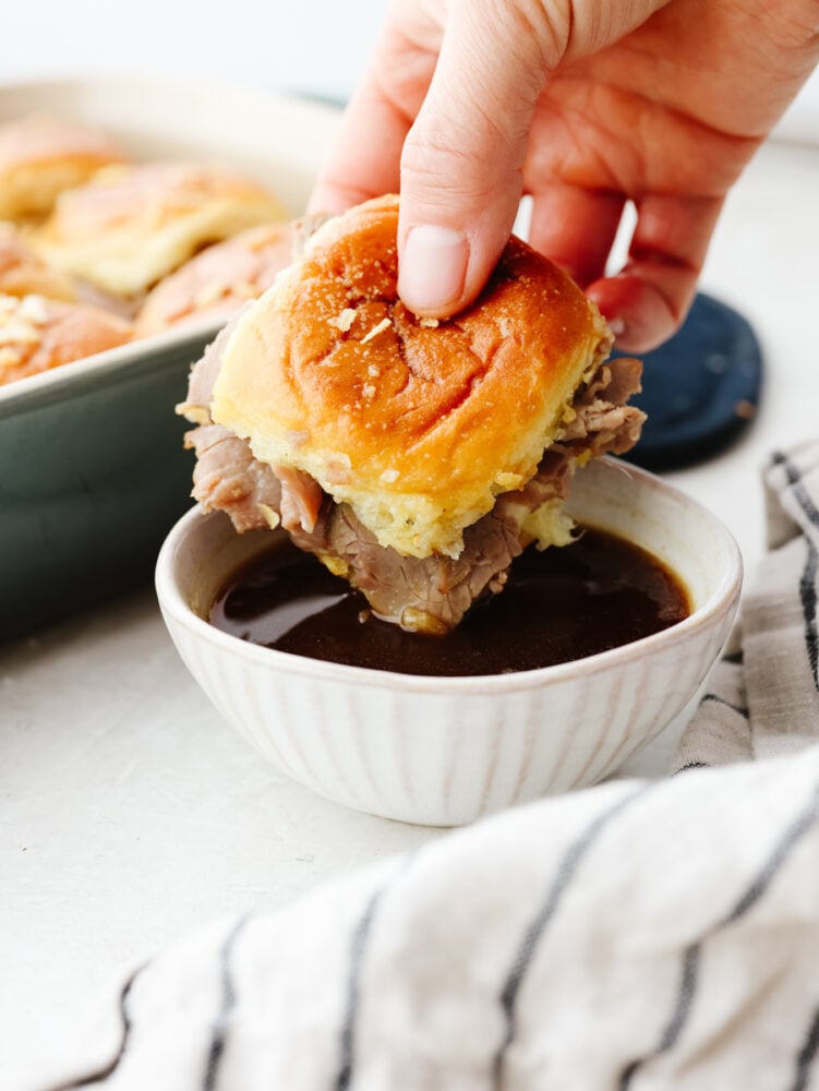 French dip sliders are filled with tender roast beef and melty provolone in bite-size form! It's a delicious pull-apart treat for a large crowd! Dipping a slider into au jus sauce.