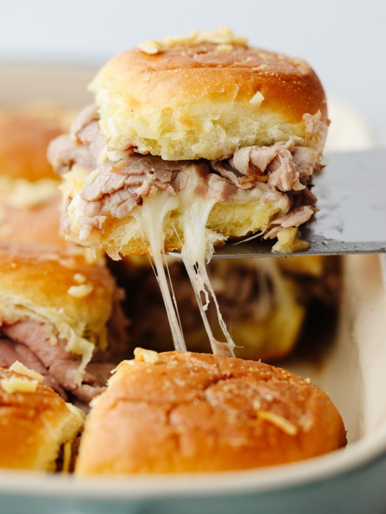 French dip sliders are filled with tender roast beef and melty provolone in bite-size form! It's a delicious pull-apart treat for a large crowd! A French dip slider being taken out of the pan.