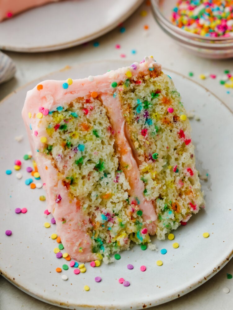 This light and fluffy homemade funfetti cake is perfect for every celebration! A white cake bursting with rainbow sprinkles is so delicious and will have everyone asking for a second slice. A slice of cake on a plate.