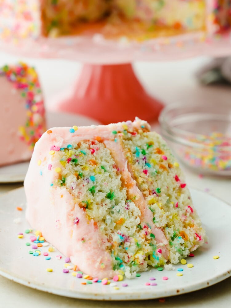 This light and fluffy homemade funfetti cake is perfect for every celebration! A white cake bursting with rainbow sprinkles is so delicious and will have everyone asking for a second slice. A slice of funfetti cake on a plate.