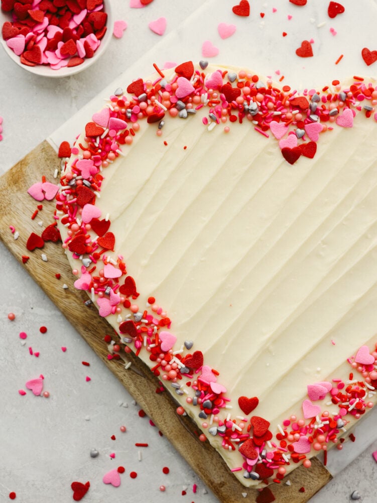 Festive and delicious, this heart-shaped cake is ready to impress your valentine! You can't go wrong with a red velvet cake topped with luscious cream cheese frosting! A whole cake on a wooden platter.